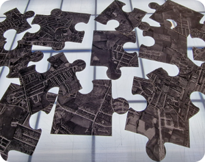 Disassembled jigsaw puzzle pieces displaying printed aerial map imagery.