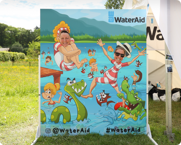 People posing behind a WaterAid branded photo cutout board at an outdoor event.